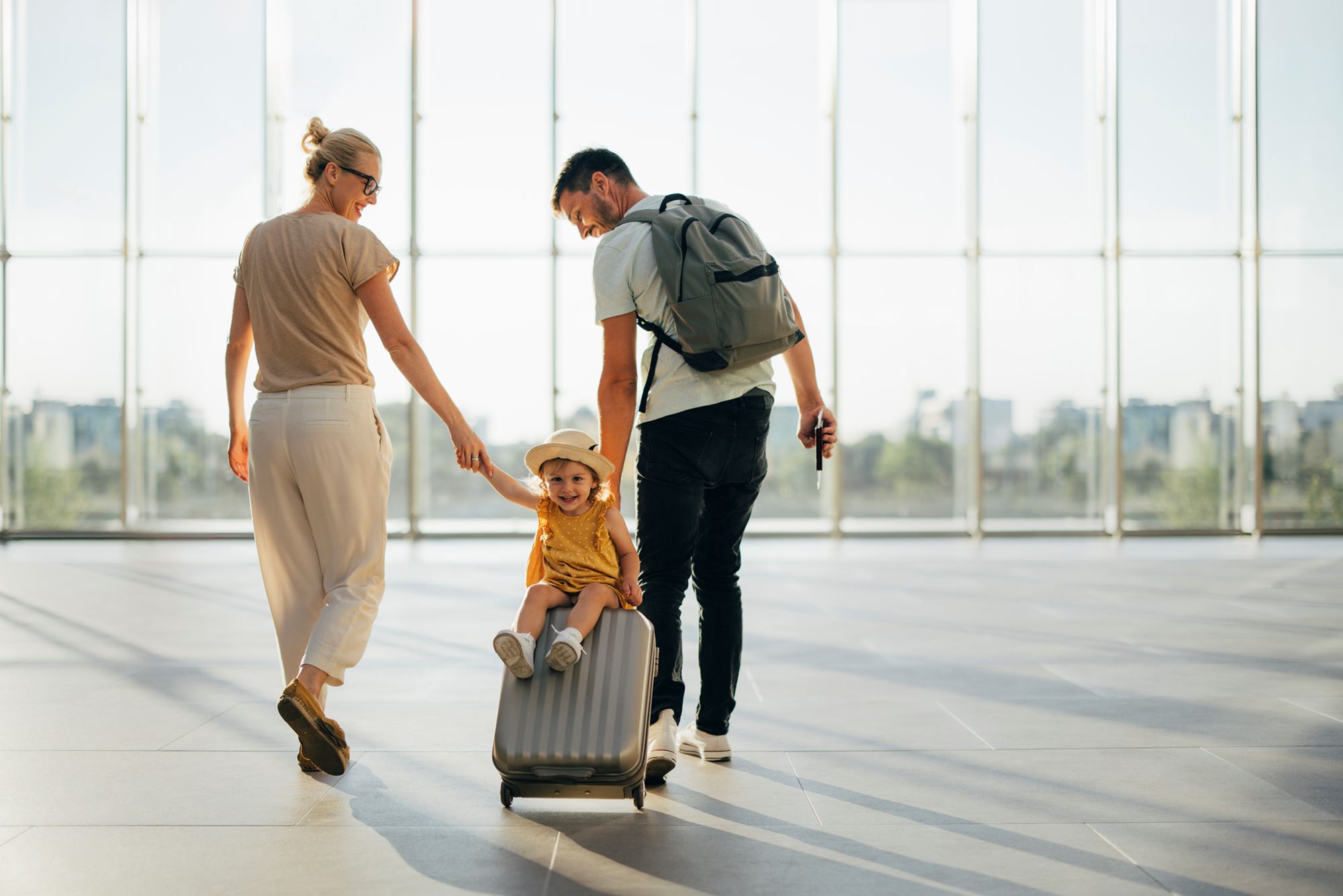 Young family travelling through airport with child sitting on their luggage